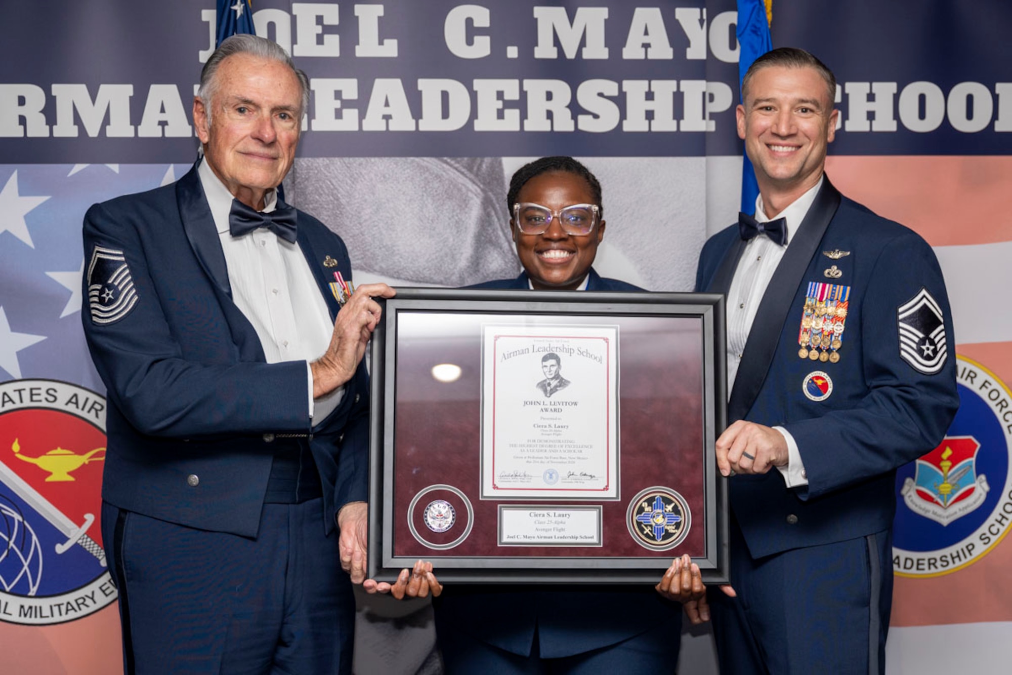 U.S. Air Force Senior Airman Ciera Laury, center, Airman Leadership Graduate, accepts the John L. Levitow Award from Retired Chief Master Sgt. Richard McElderry, left, and Master Sgt. Justin Tite, during the graduation of Joel C. Mayo ALS Class 25-A at Holloman Air Force Base, New Mexico, Nov. 21, 2024. The John L. Levitow Award is presented to the student demonstrating the highest level of leadership and scholastic performance and is partially determined by the assignment of points by their peers. (U.S. Air Force photo by Airman 1st Class Michelle Ferrari)