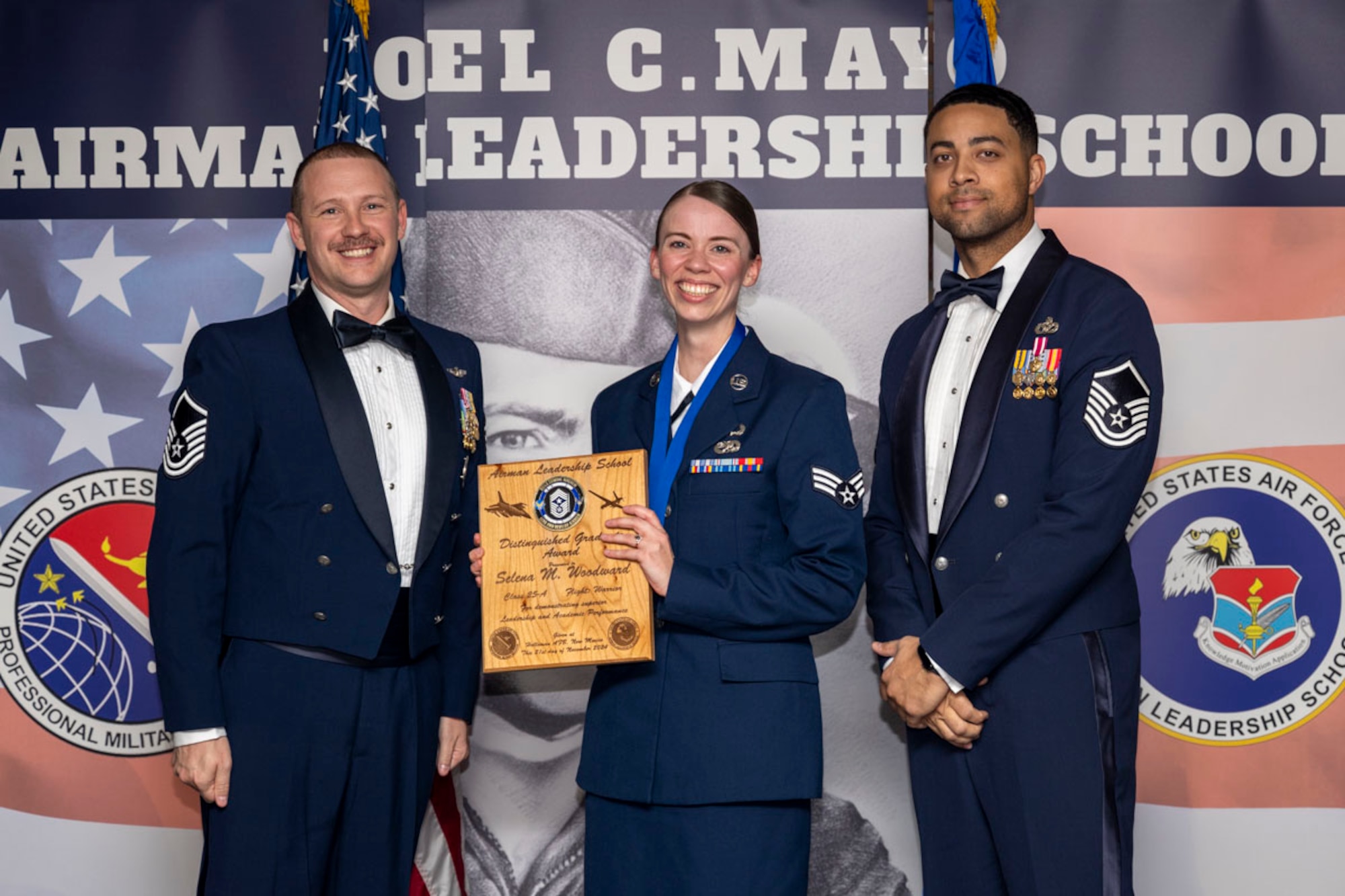 U.S. Air Force Senior Selena Woodward, center, Airman Leadership Graduate, accepts the Distinguished Graduate Award from Master Sgt. Chaz Lineberger and Master Sgt. Nicholas Booker during the graduation of Joel C. Mayo ALS Class 25-A at Holloman Air Force Base, New Mexico, Nov. 21, 2024. The distinguished graduate award is presented to the top 10% of graduates for their performance in academic evaluations and demonstration of leadership. (U.S. Air Force photo by Airman 1st Class Michelle Ferrari)