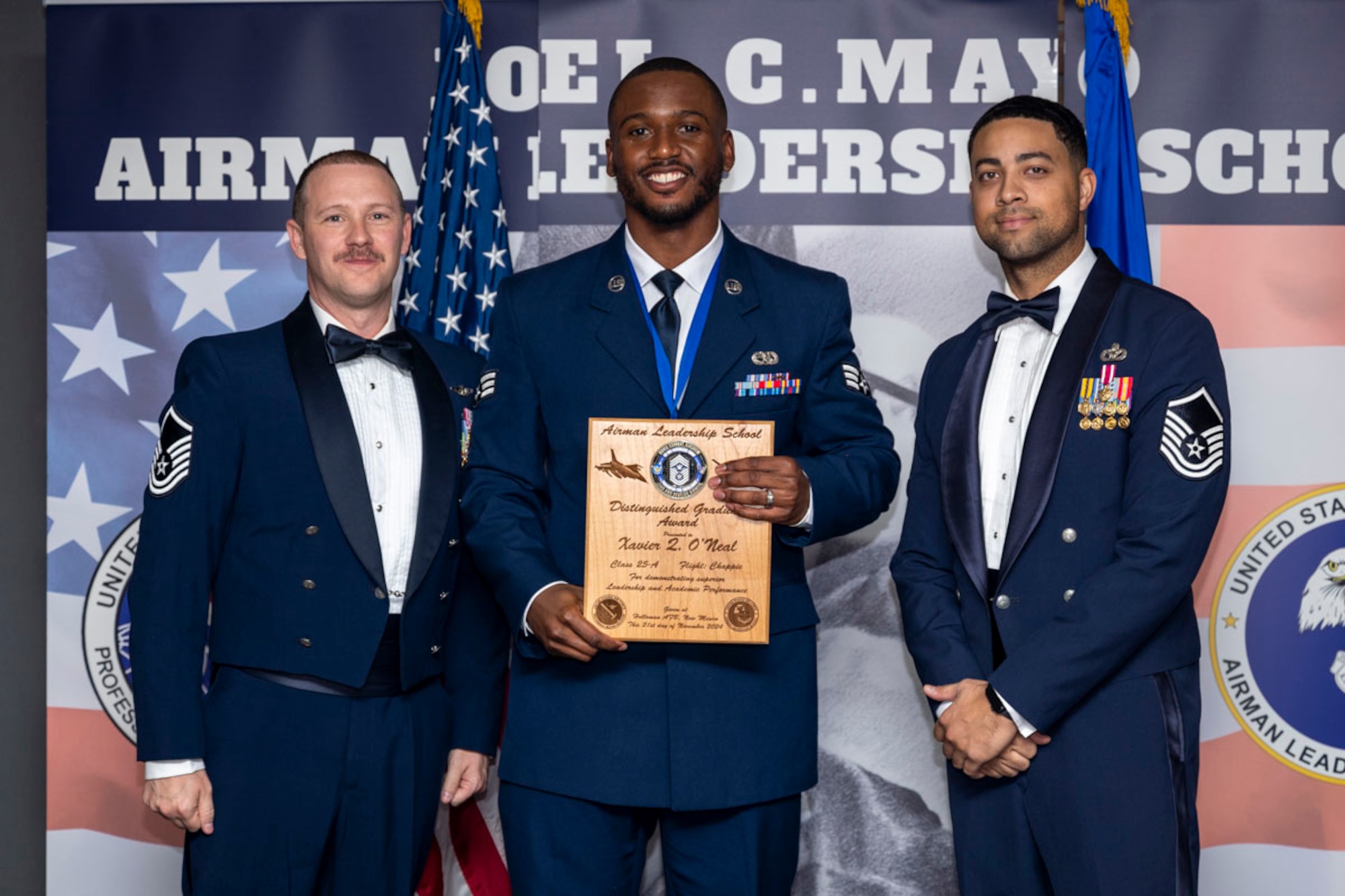 U.S. Air Force Senior Airman Xavier O’Neal, center, Airman Leadership Graduate, accepts the Distinguished Graduate Award from Master Sgt. Chaz Lineberger and Master Sgt. Nicholas Booker during the graduation of Joel C. Mayo ALS Class 25-A at Holloman Air Force Base, New Mexico, Nov. 21, 2024. The distinguished graduate award is presented to the top 10% of graduates for their performance in academic evaluations and demonstration of leadership. (U.S. Air Force photo by Airman 1st Class Michelle Ferrari)