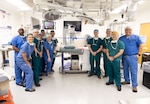 Surgeons wearing scrubs stand around machine in operating room.