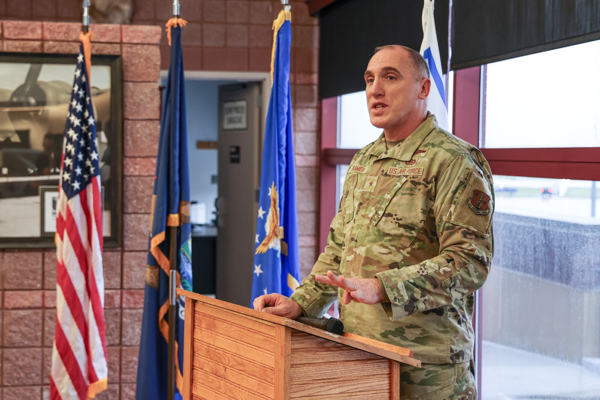 Uniformed Air Force officers stands behind podium, holding microphone.