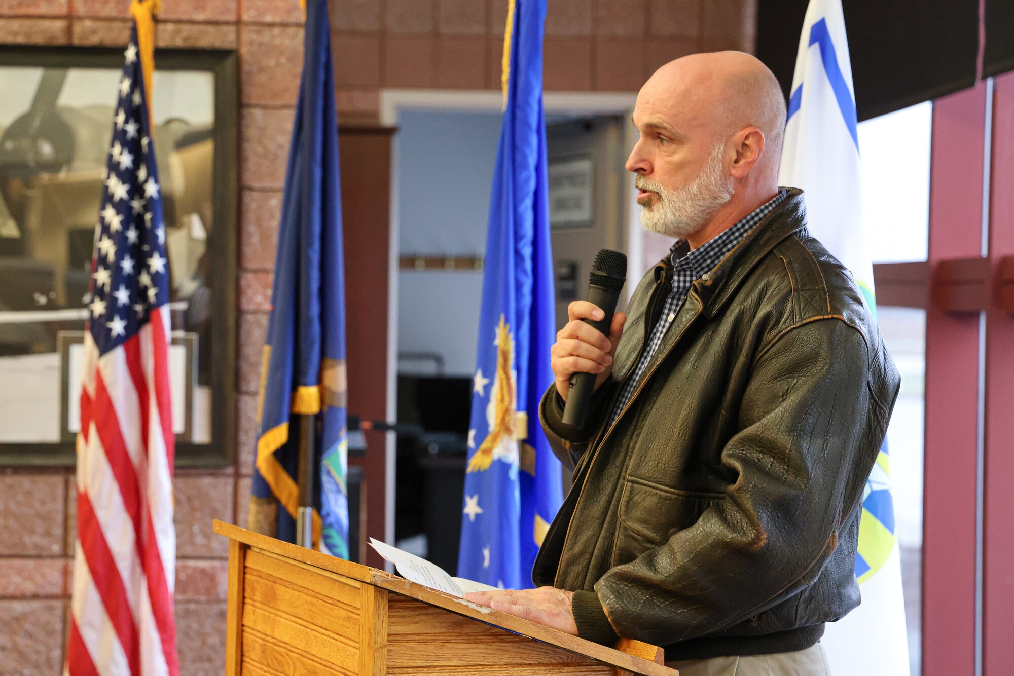 Man in civilian clothes stands at podium, holding microphone.
