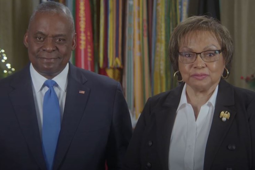 A screengrab of the secretary of defense and his wife standing next to each other in front of a flag.