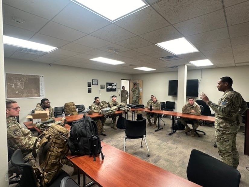 A group of guardians and airmen sit around a table in a classroom.