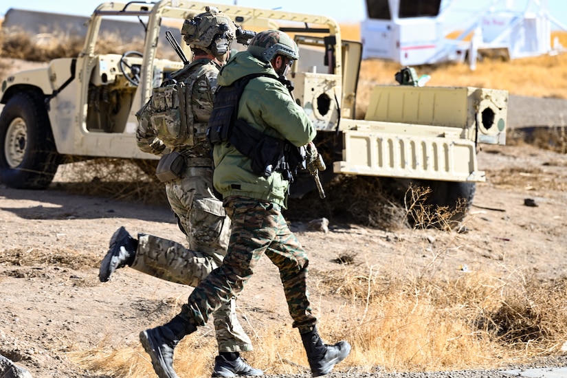 Soldiers run in desert area near a parked vehicle.