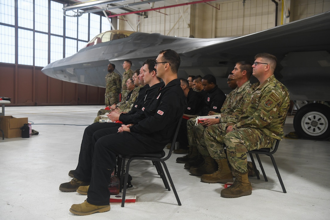 Group of Airmen sitting in chairs in front of F-22 Raptor.