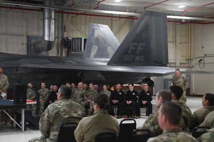 View of the audience and members sitting in chairs in front of F-22 Raptor