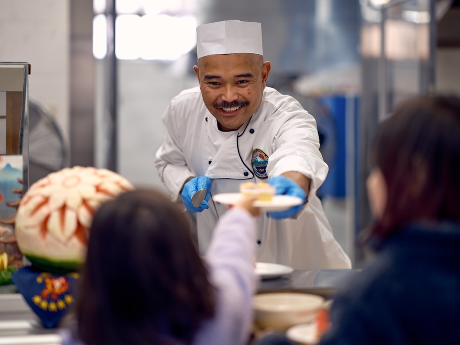 Culinary Specialist 1st Class Alvic Dedios of Commander, Fleet Activities Yokosuka, serves a slice of cake to a child at the Commodore Matthew C. Perry General Mess during an Open Galley Event to serve Thanksgiving meals to the Commander, Fleet Activities Yokosuka base community members Thursday, November 28.