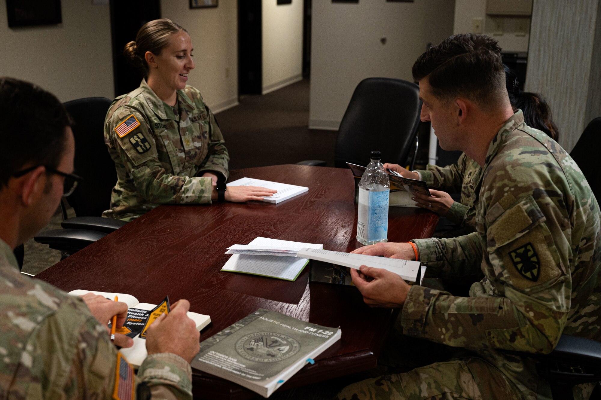 A group of soldiers sit at a conference table with notebooks and documents on the tabletop.