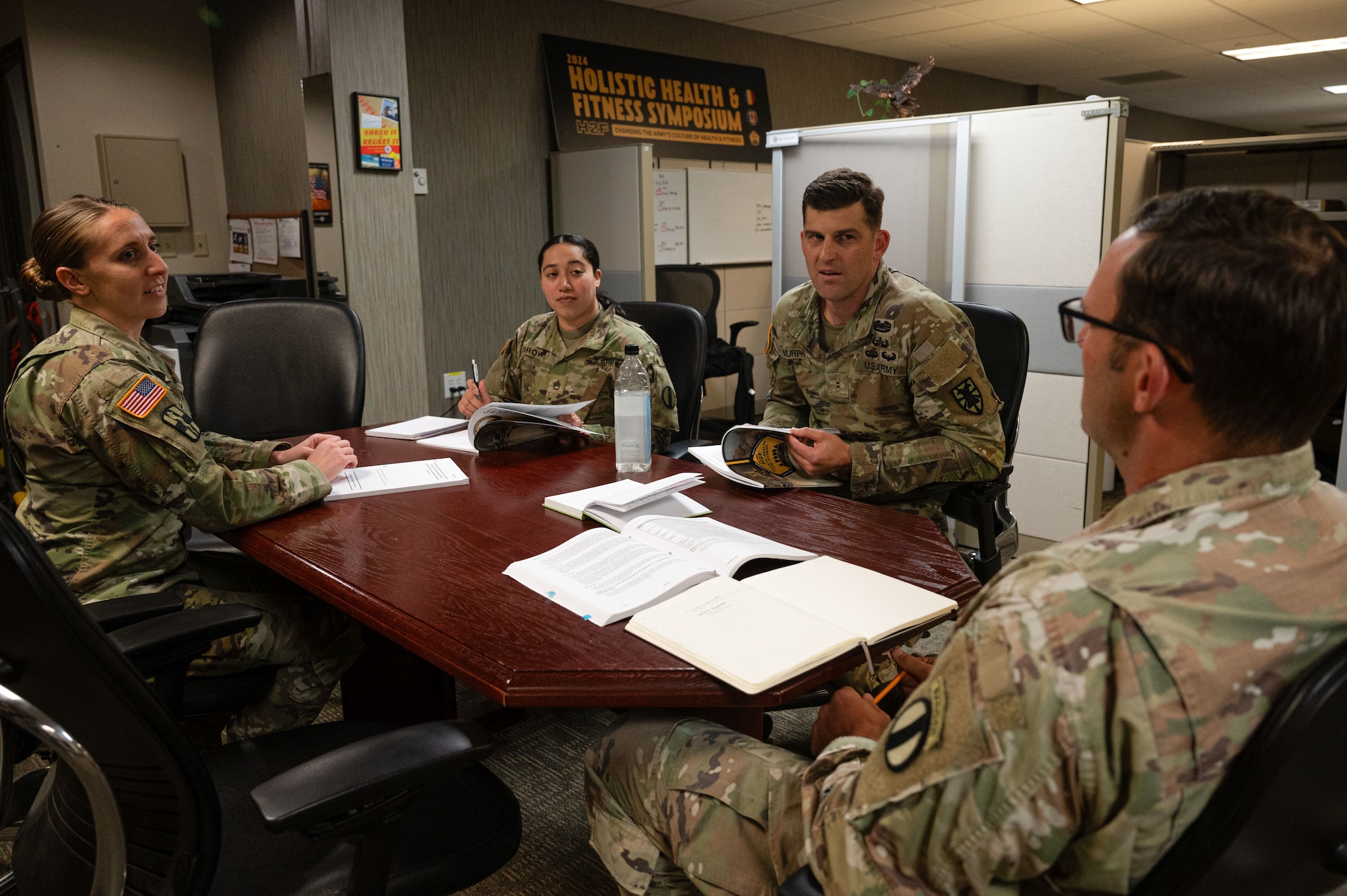 A group of soldiers sit at a conference table with open notebooks in front of them.