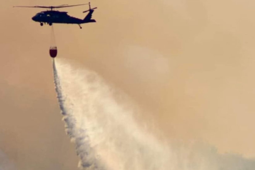 A helicopter pours a bucket of water on a fire.