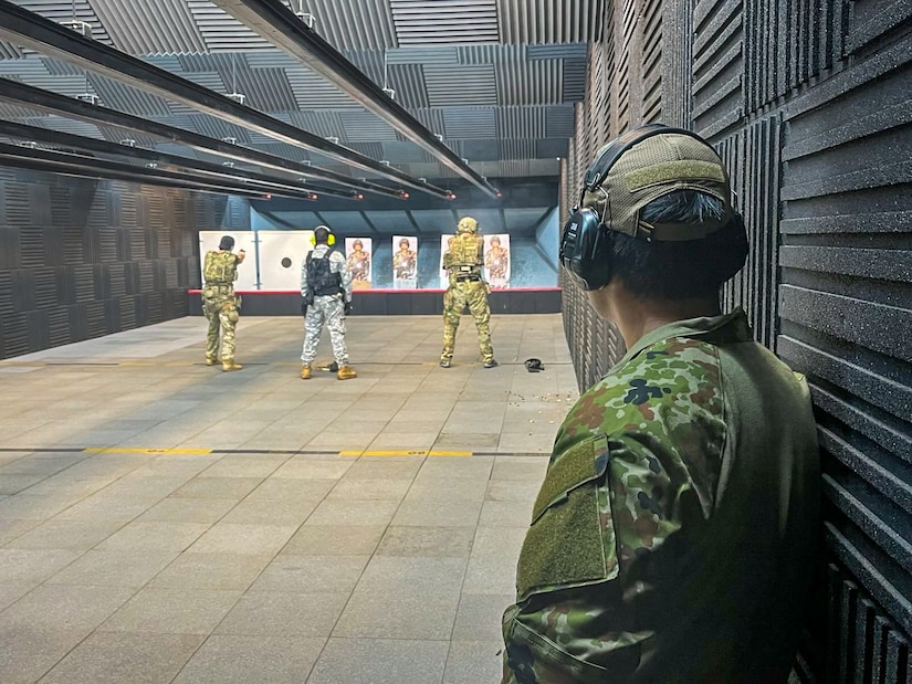 Service members conduct target practice as a fellow service member watches.