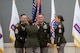 Soldier in dress uniform accepts Recruiting Brigade flag with streamers from another soldier while two others look on.