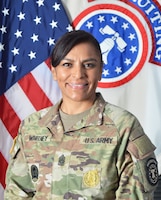 Female Soldier in uniform smiles while standing in front of United States and Army Recruiting Flags