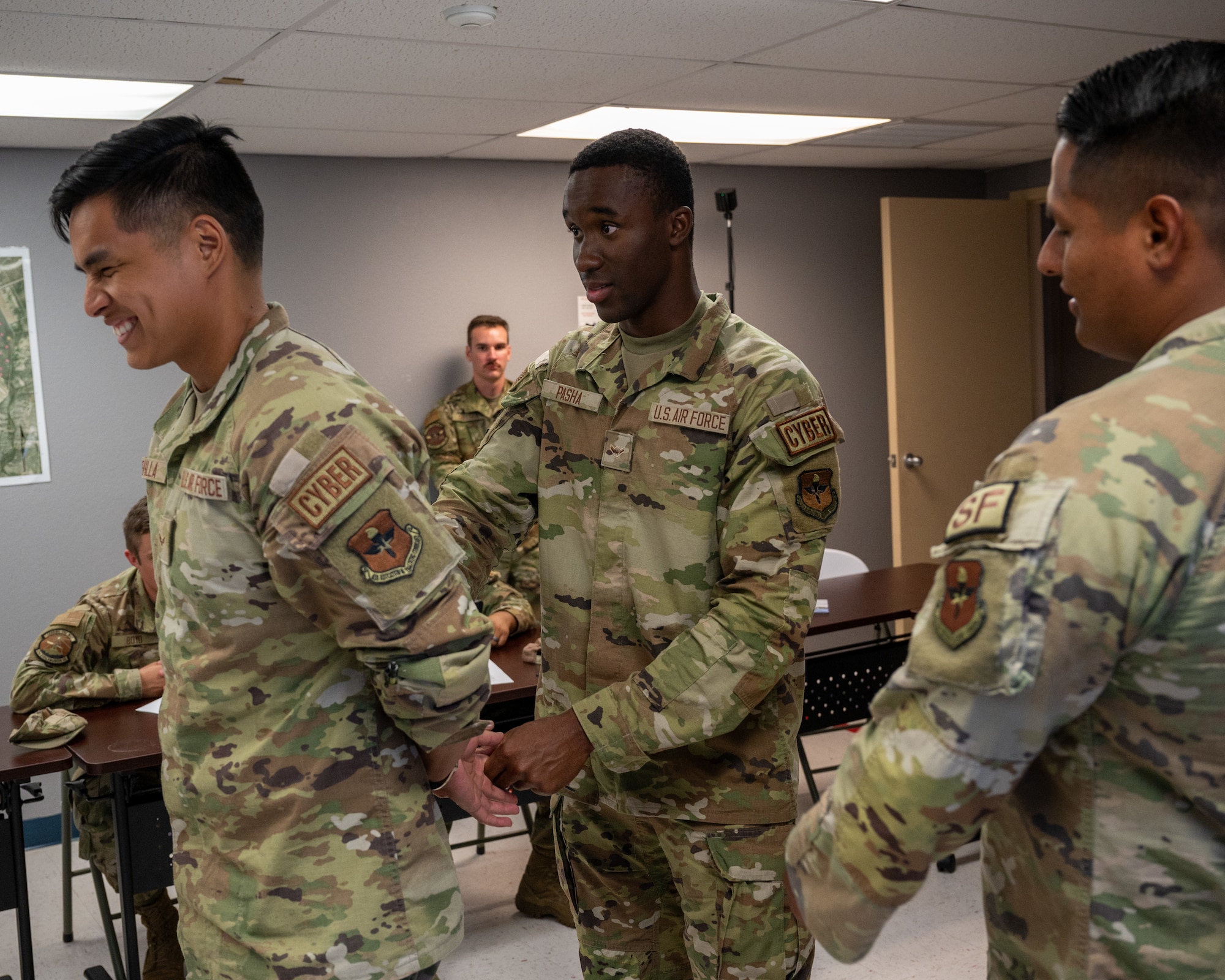 U.S. Air Force Airman 1st Class Dante Sevilla, left, 47th Communication Squadron (CS) security forces augmentee, is put in handcuffs by Airman Sunnah Pasha, middle, 47th CS security forces augmentee under the supervision of  Senior Airman Jose Moreno, right, 47th Security Forces Squadron trainer, at Laughlin Air Force Base, Texas Aug. 21, 2024. Augmentees learn essential parts of the security forces operations to be able to support thier mission, allowing them to assist during crisis periods. (U.S. Air Force photo by Staff Sgt. Nicholas Larsen)