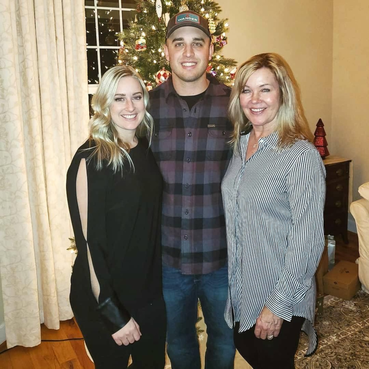 Three people pose in front of a Christmas tree while in a room.
