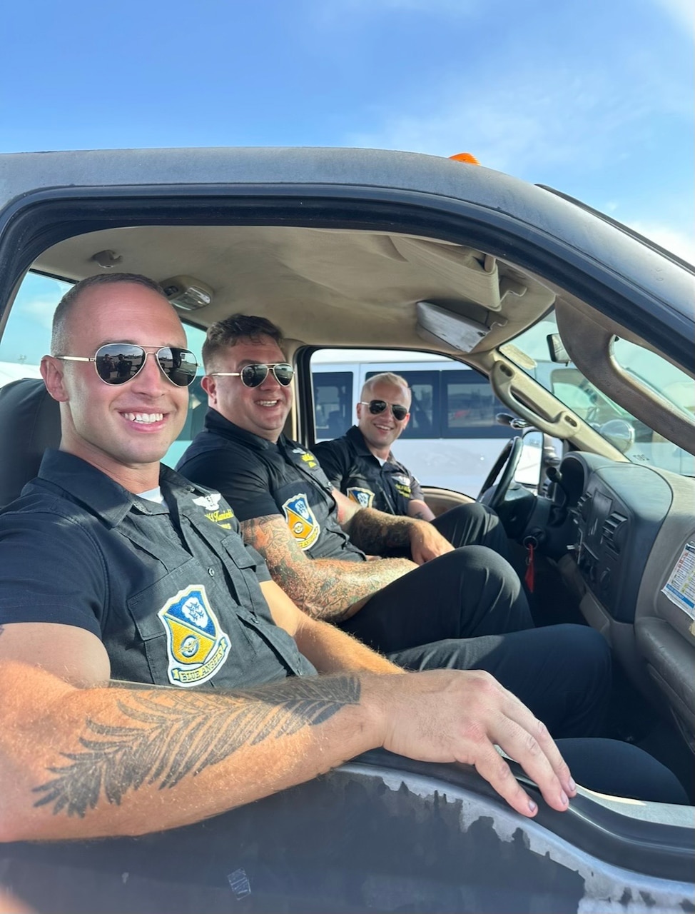 Three sailors wearing Blue Angels uniform pose while seated in a truck.