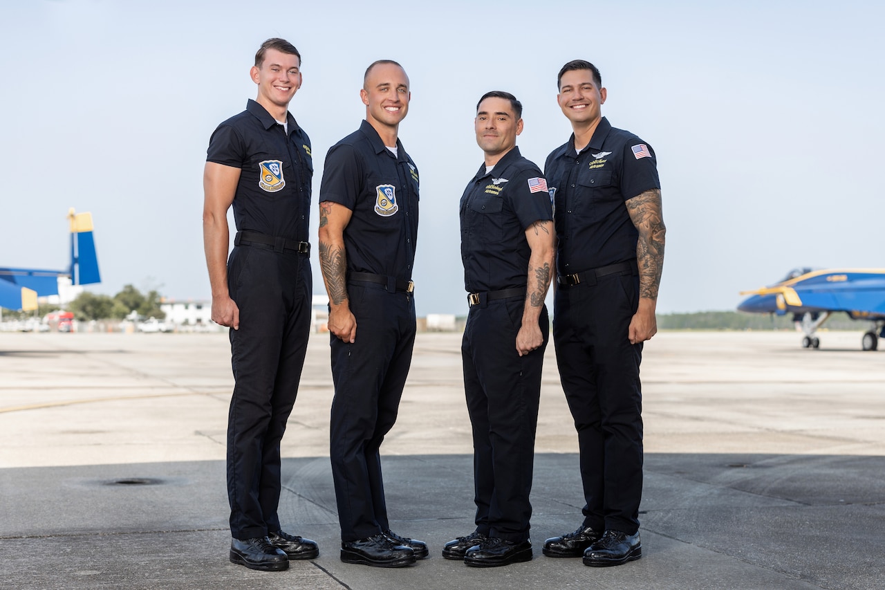 Four male service members pose for a photo with a blue and gold military aircraft in the background.