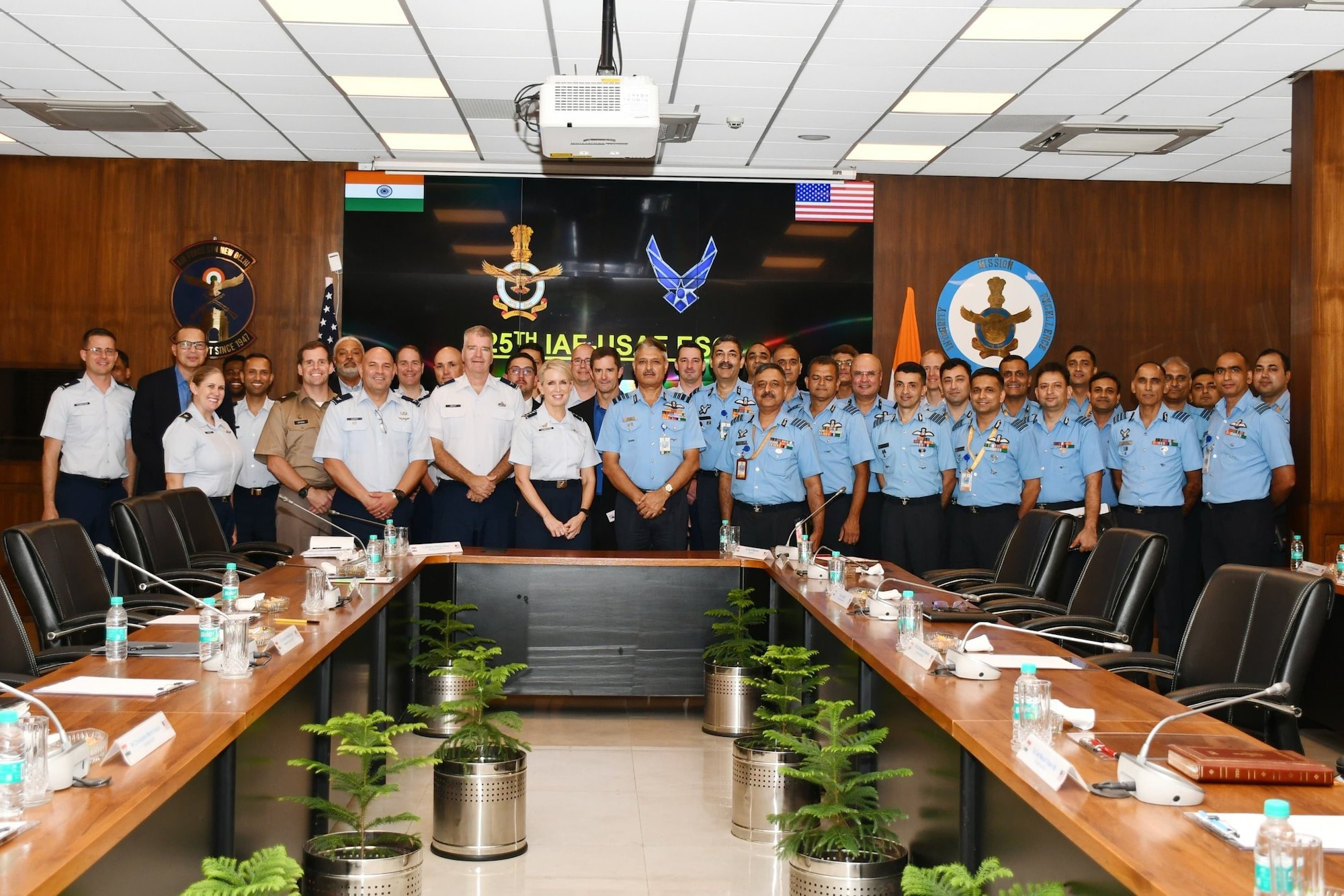 Forty people in formal military attire line up in two rows in front of a conference room table.