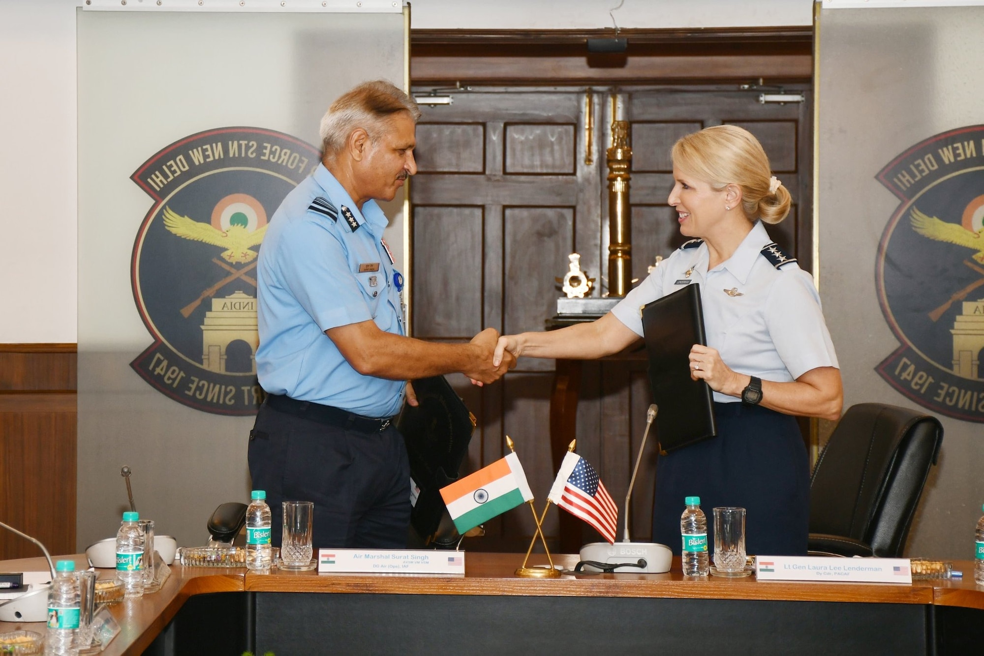 A woman in formal military attire shakes hands with a man in formal military attire in a military conference room.