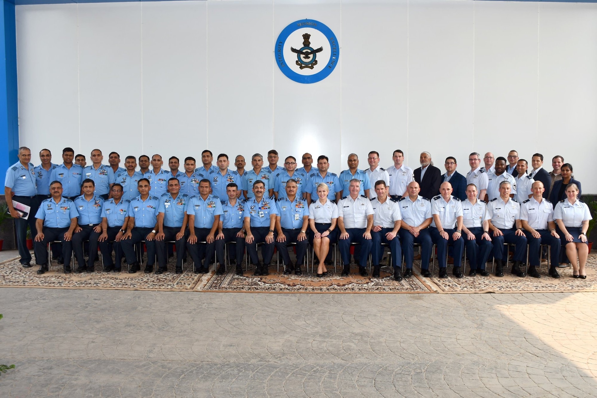 Forty people in military formal military uniform form two lines in a large, bare room.