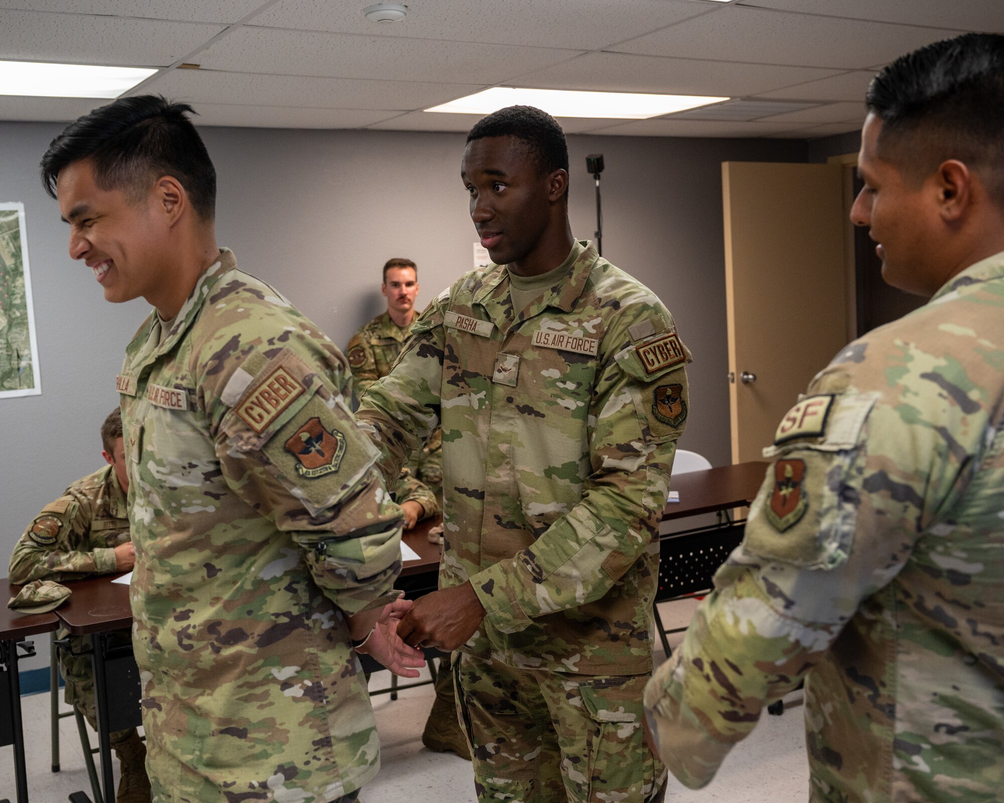 U.S. Air Force Airman 1st Class Dante Sevilla, left, 47th Communication Squadron (CS) security forces augmentee, is put in handcuffs by Airman Sunnah Pasha, middle, 47th CS security forces augmentee under the supervision of  Senior Airman Jose Moreno, right, 47th Security Forces Squadron trainer, at Laughlin Air Force Base, Texas Aug. 21, 2024. Augmentees learn essential parts of the security forces operations to be able to support thier mission, allowing them to assist during crisis periods. (U.S. Air Force photo by Staff Sgt. Nicholas Larsen)