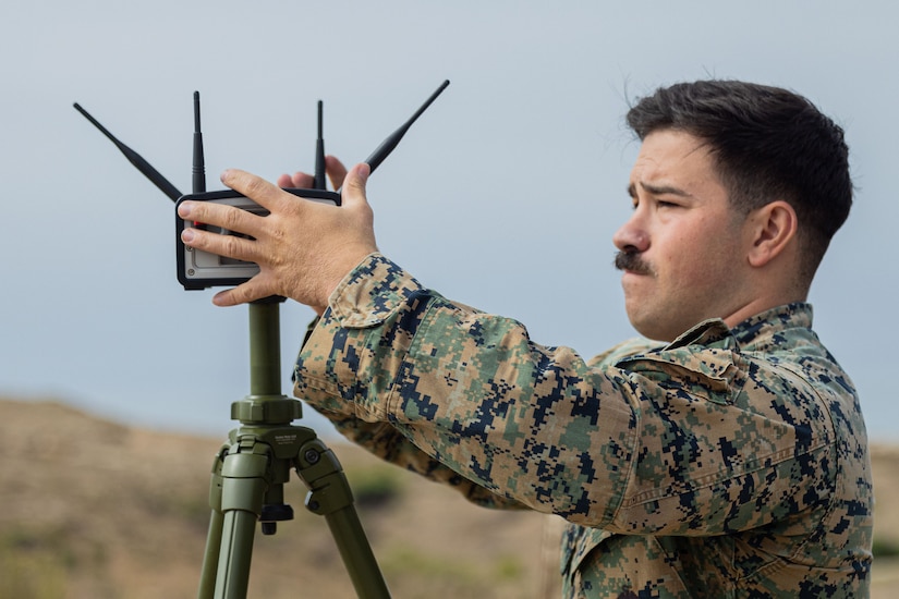 A Marine tinkers with a tripod equipment outside.