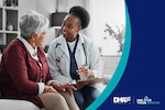 Doctor wearing white coat sits on a couch next to an elderly patient and shows her a clipboard.