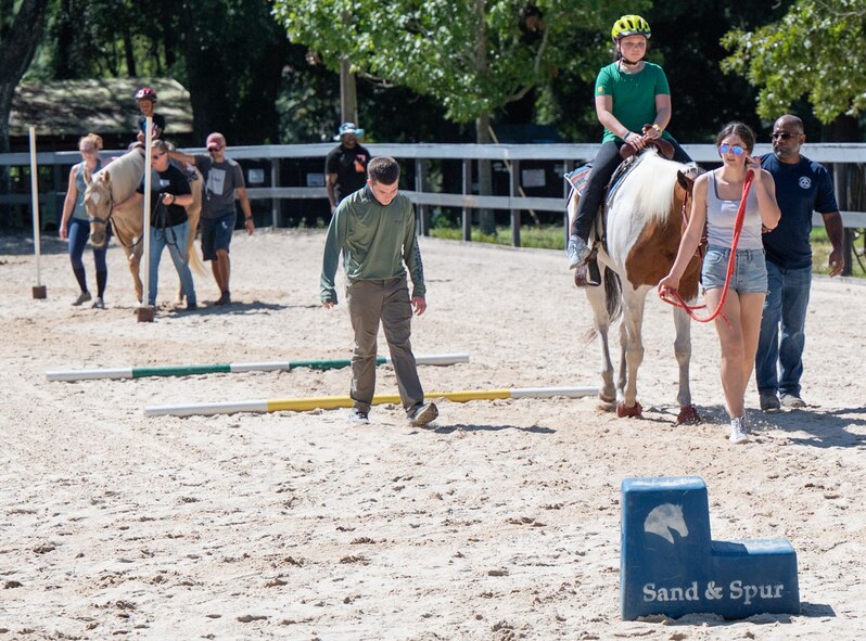 Families and Sand and Spur Riding Club members guide horses around a field.
