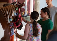 A couple teens pet a horse on the snout.