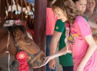 A pony gives a kiss on a young girl's hand.