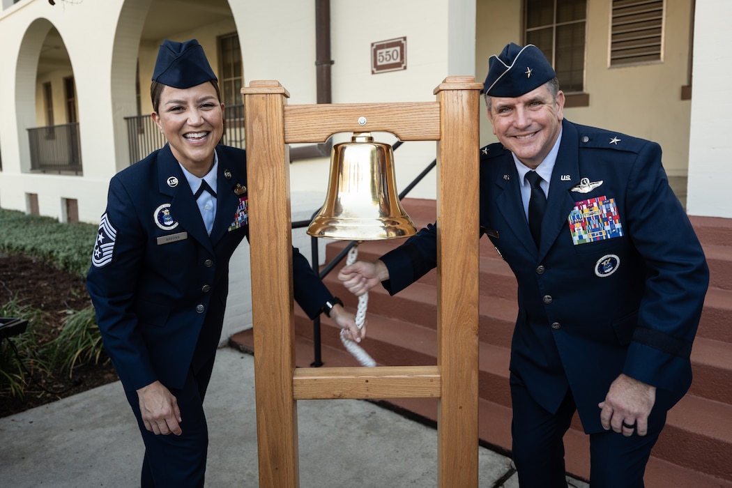 Man and woman stand next to bell in unifrom