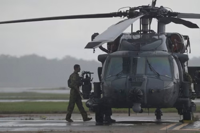 An airman walks toward a helicopter parked on the tarmac on an overcast day.