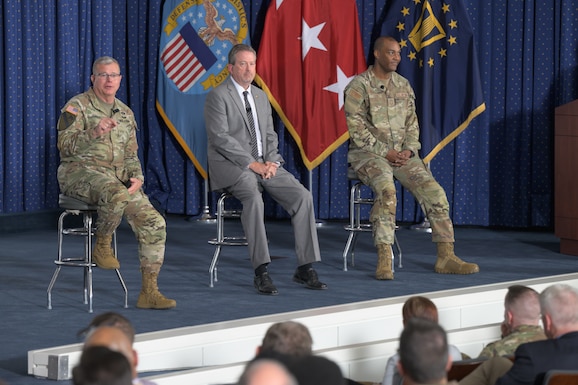 Three men sit on stools on a stage