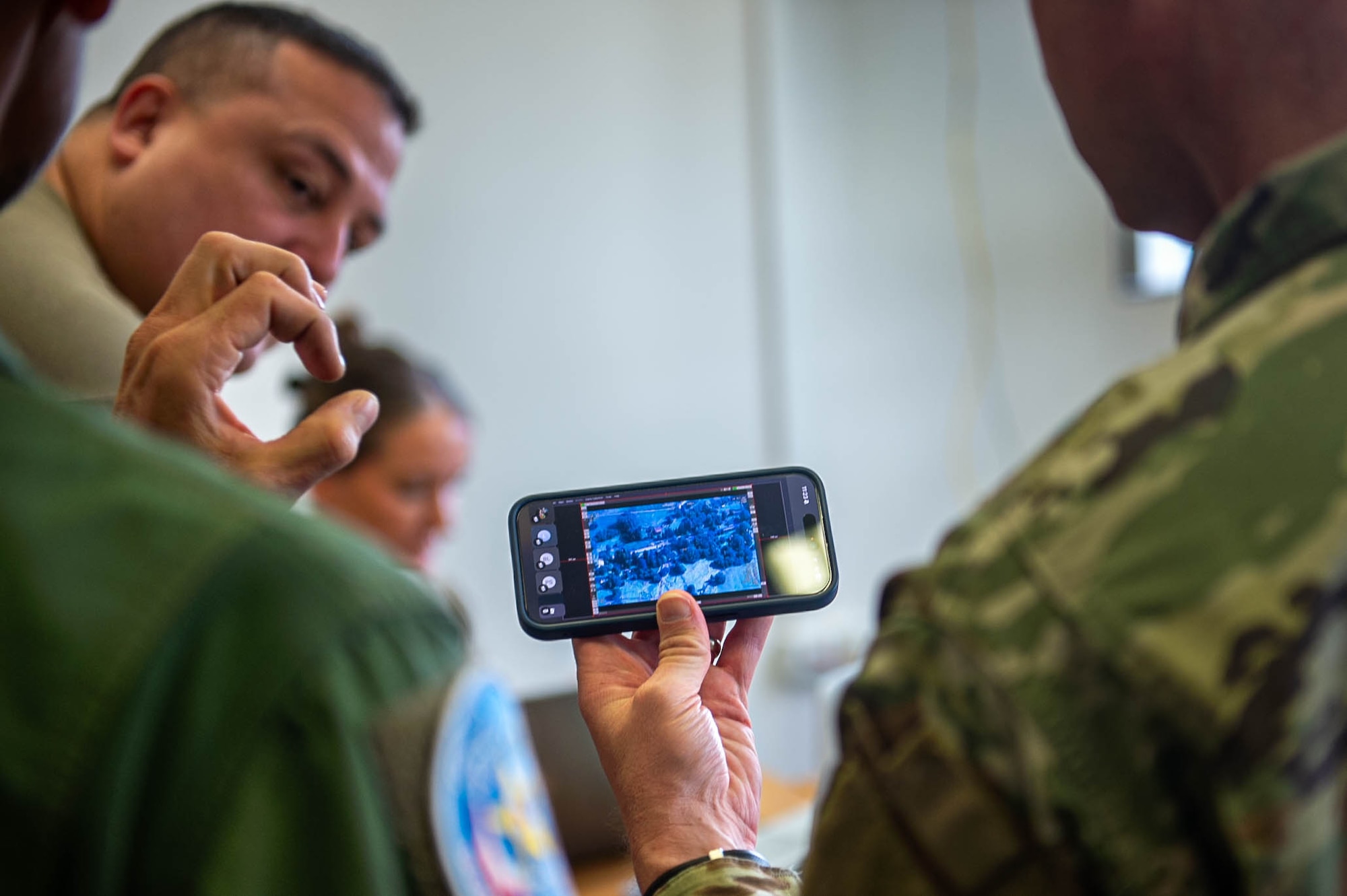 Over-the-shoulder view of two people reviewing aerial footage of flood damage on a smart phone.