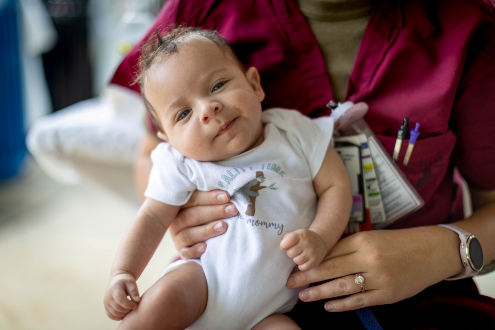 Nurse holds infant in onesie in her arm.