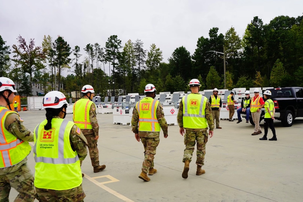 A group of USACE employees walk towards a set of Generators which are prepared for deployment to areas in North Carolina impacted by Hurricane Helene