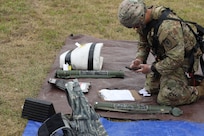 A Soldier kneels down and looks at a smart phone while working with training aides representing enemy munitions.