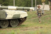 A Soldier carrying a pink marking flag approaches a T-72 main battle tank.