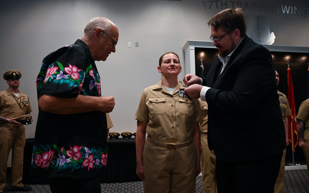 U.S. Navy Cryptologic Technician Interpretive Chief Petty Officer Deborah Bowers, Information Warfare Training Command Monterey Detachment Goodfellow instructor, stands at attention while her husband, David Bowers and father, Bob Schaff, pins CPO insignia on her collar at the Fiscal Year 2025 CPO Pinning Ceremony at the Powell Event Center, Goodfellow Air Force Base, Texas, Sept. 27, 2024. During the ceremony, ten U.S. Navy Sailors pinned the rank of chief petty officer after completing the six-week CPO initiation. (U.S. Air Force photo by Airman 1st Class Evelyn J. D’Errico)