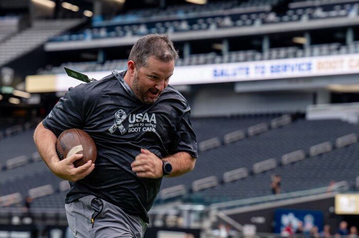 An Airman runs with a football in his hand.