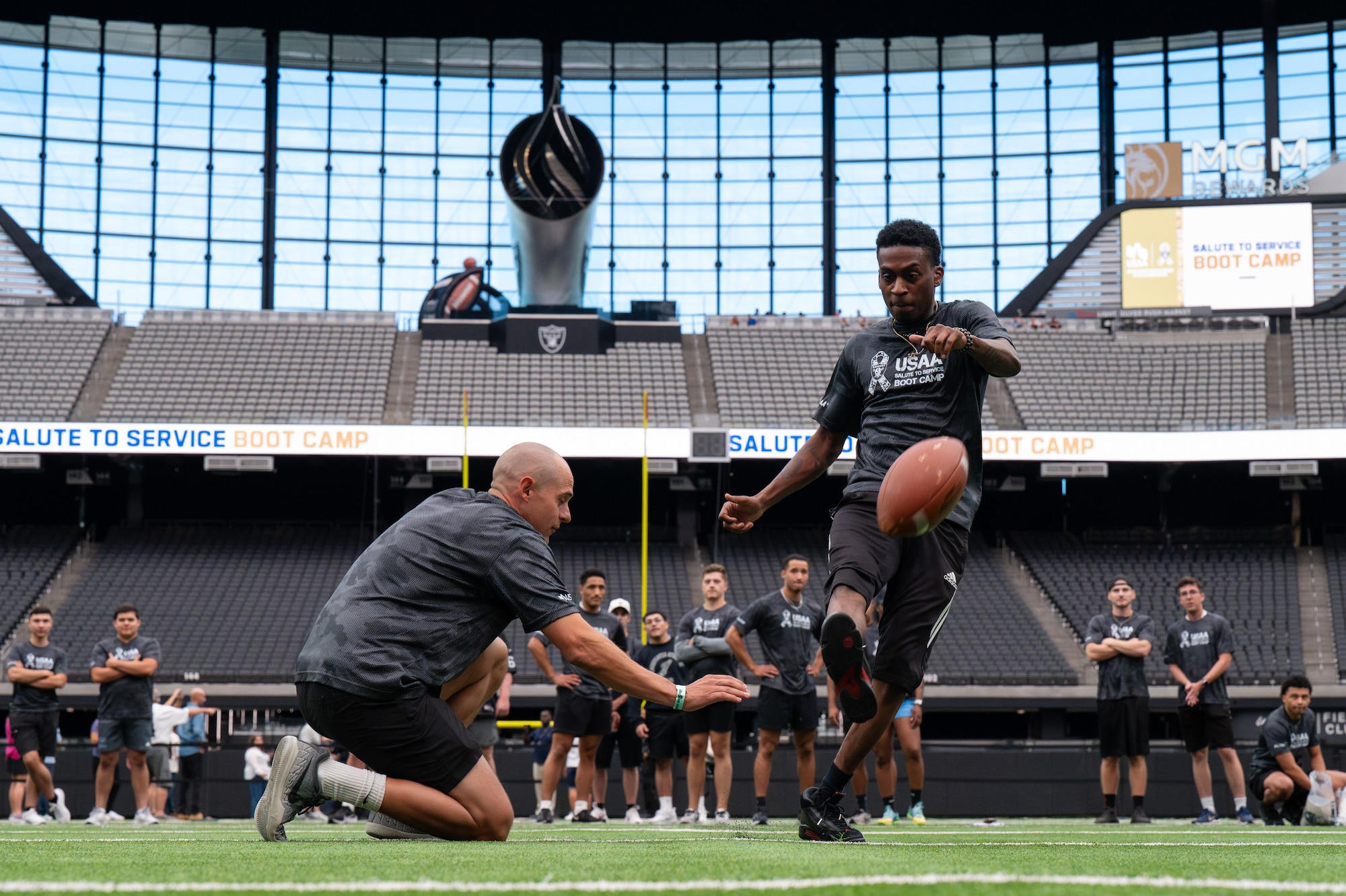 An Airman kicks a football on a football field.