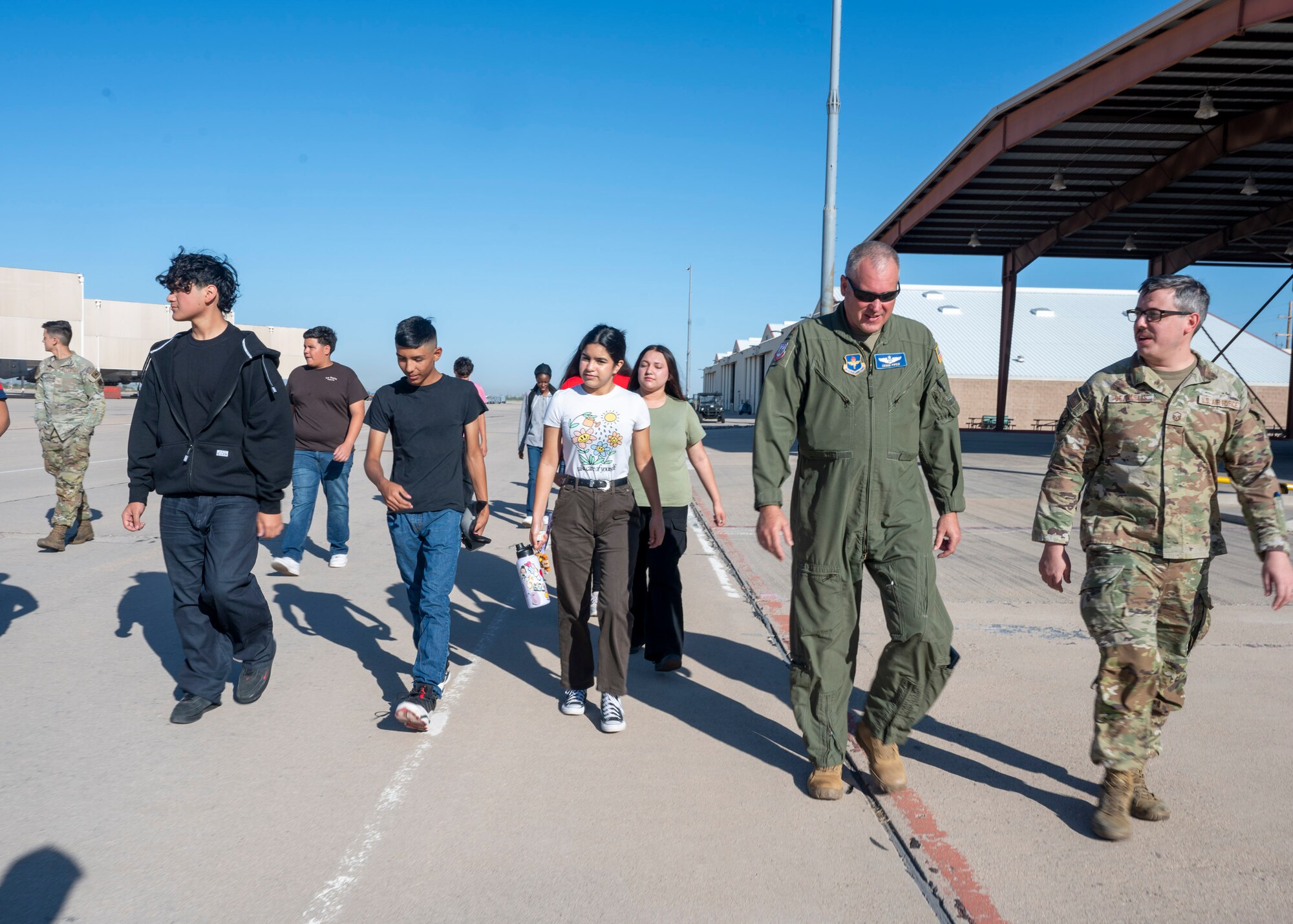 U.S. Airmen walk with Air Force Junior Reserve Officer Training Corps students on a flightline.