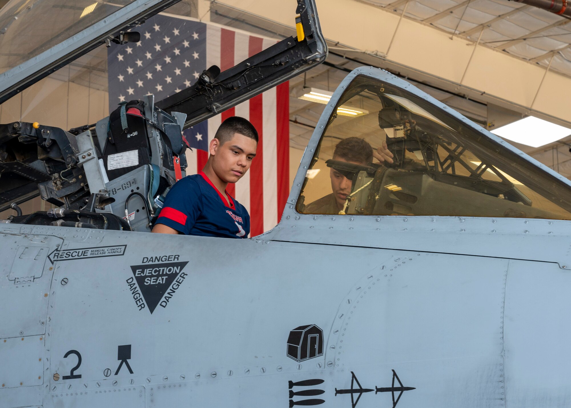 An Air Force Junior Reserve Officer Training Corps student sits in an A-10C Thunderbolt II aircraft while a U.S. Airman watches.