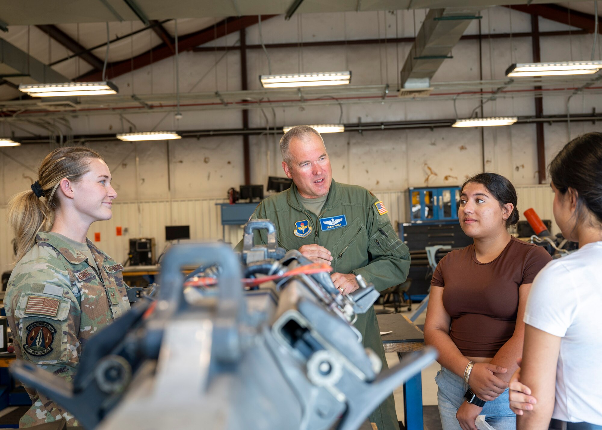 U.S. Airmen speak with Air Force Junior Reserve Officer Training Corps students while standing next to a piece of aircraft equipment.
