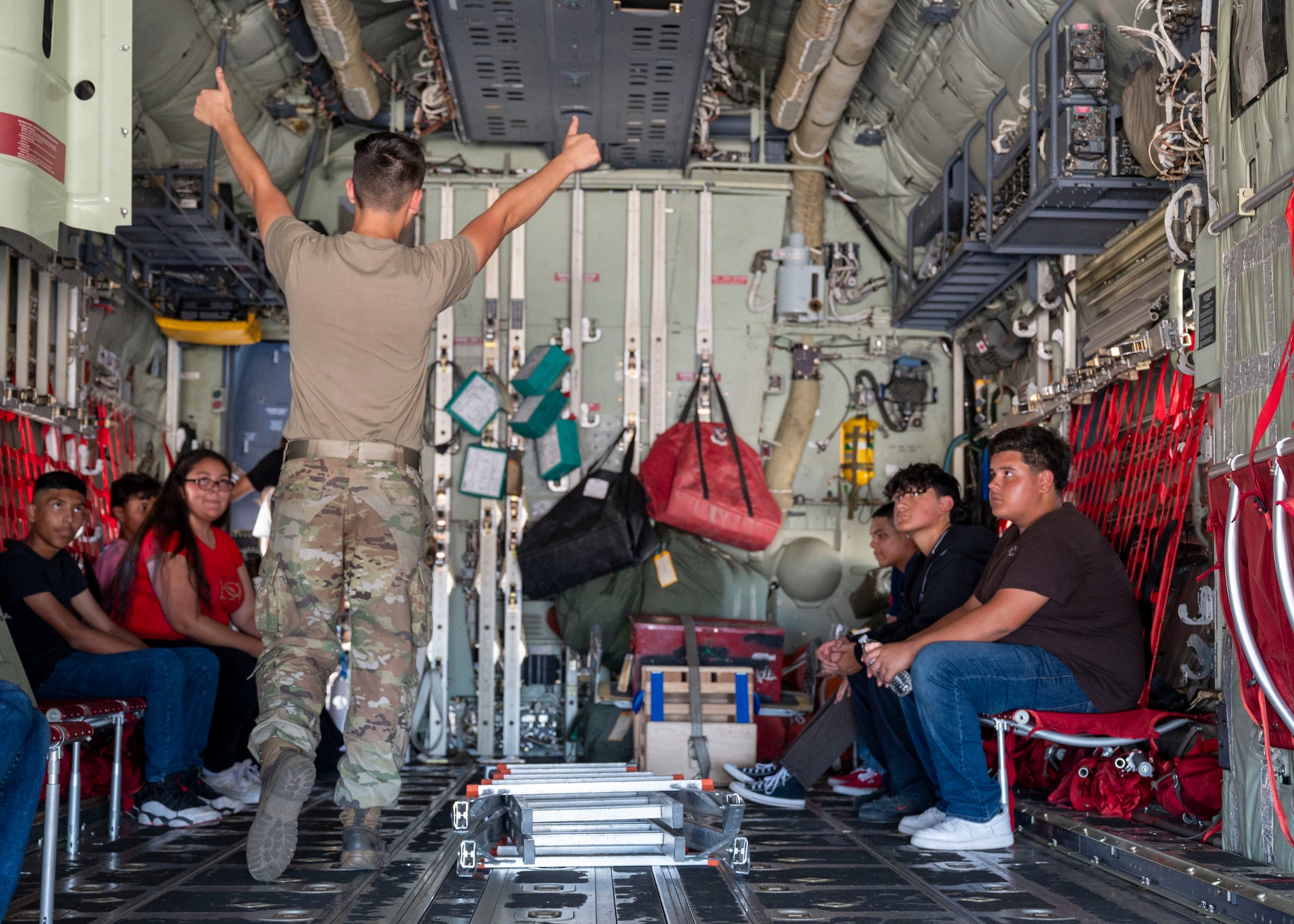 A U.S. Airmen points inside of the back of an HC-130J Combat King II while Junior Reserve Officer Training Corps students watch.