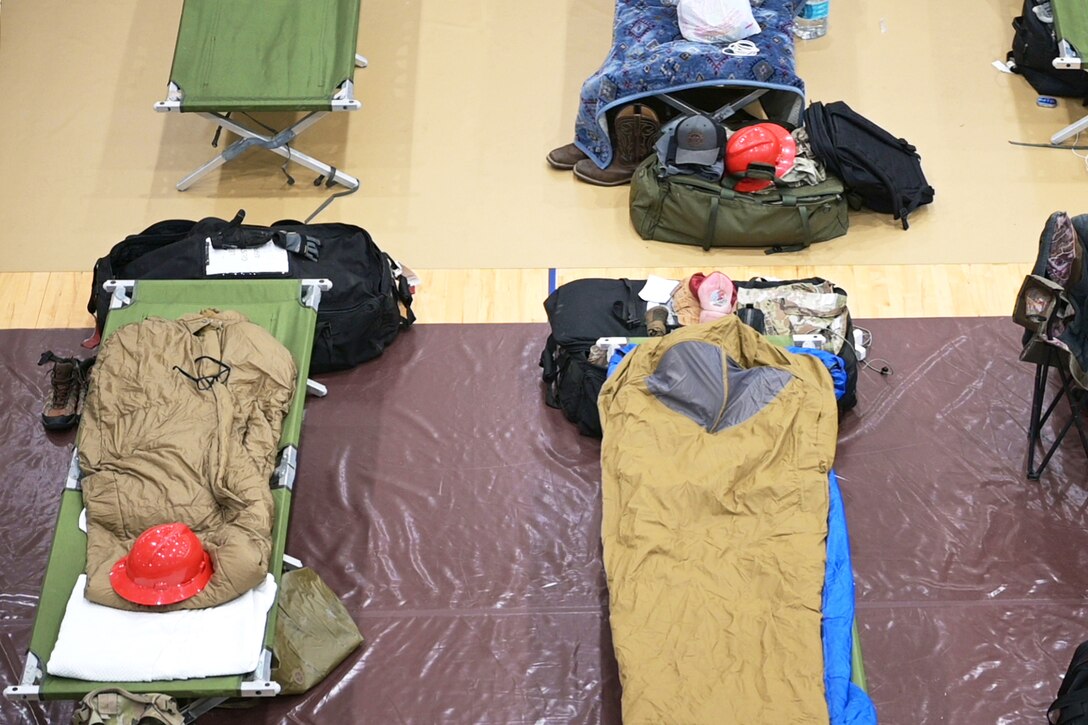 Suitcases sit next to cots in a fitness center as seen from above.