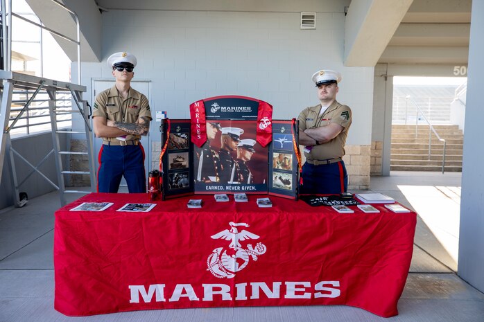 U.S. Marine Corps Cpl. Gabriel Peavey, left, and Cpl. Matthew Williams, both recruiters with Recruiting Sub Station Spring, Recruiting Station Houston, pose for a photo behind a recruitment table display during the Bands of America North Houston Regional Championship at Woodforest Bank Stadium in Shenandoah, Texas, Sept. 28, 2024. The Marines set up a recruitment table display and awarded high school bands for their performances. (U.S. Marine Corps photo by Sgt. Ryan H. Pulliam)