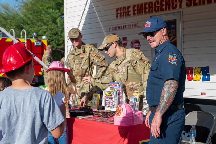 U.S. Air Force 355th Civil Engineer Squadron firefighters speak with members of the community at Davis-Monthan Air Force Base, Arizona, Oct. 1, 2024. A table was set up to raise awareness and inform the community of fire safety practices. (U.S. Air Force photo by Airman 1st Class Jasmyne Bridgers-Matos)