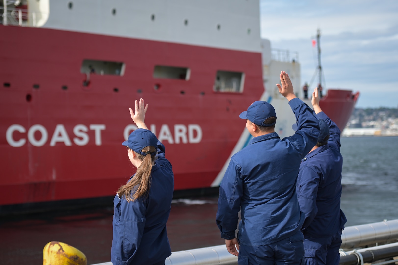 Coast Guard members from Base Seattle wave to the crew of U.S. Coast Guard Cutter Healy (WAGB 20) as the icebreaker departs Seattle, Oct. 1, 2024. The crew is scheduled to deploy on a several month operation to conduct scientific research in the northern latitudes. (U.S. Coast Guard photo by Petty Officer 1st Class Steve Strohmaier)